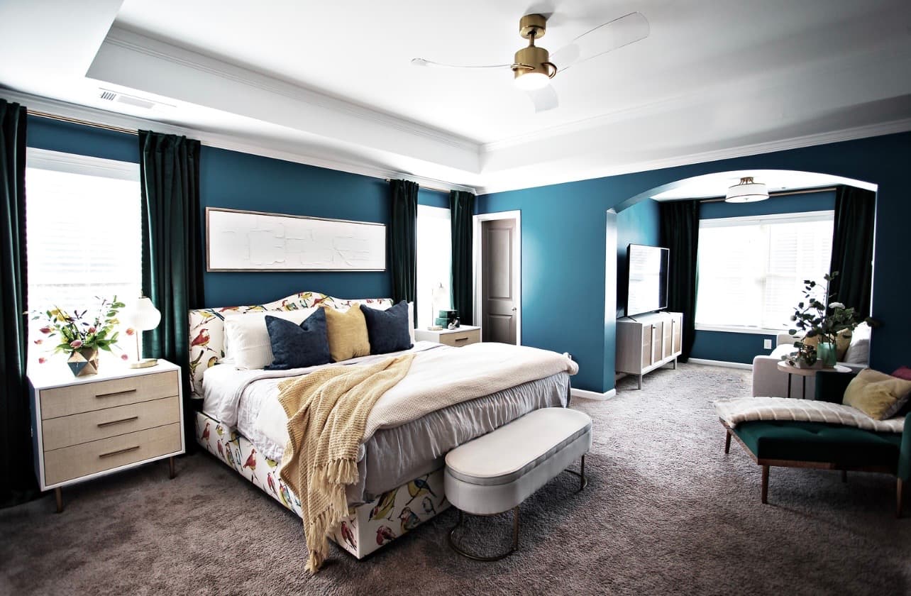 Modern bedroom with teal walls, bird-patterned bed, white bedding, and a separate sitting area.